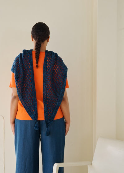 Blue shawl with bokeh pattern and tassels, draped over an orange shirt and blue pants, viewed from the back.