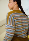 Back view of a striped sweater in mustard yellow, white, light blue, and grey, worn with braided hair.
