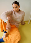 Light-colored knitted sweater paired with bright orange pants, blue socks, and white sneakers, seated on a yellow floor.