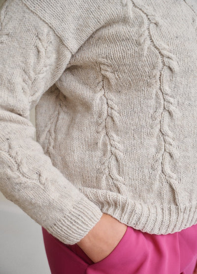Light gray cable-knit sweater with ribbed cuffs and hem, paired with bright pink pants.