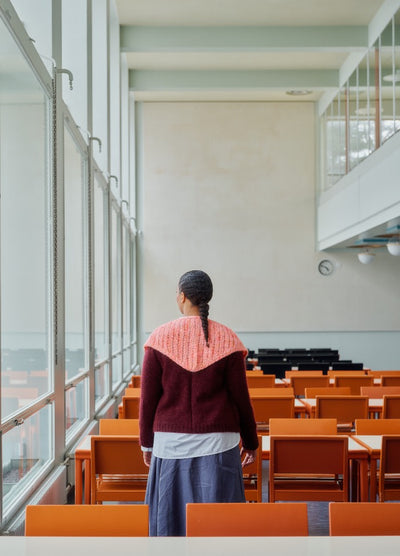 Pink shawl draped over a maroon sweater, worn in a sunlit room with orange chairs and tables.