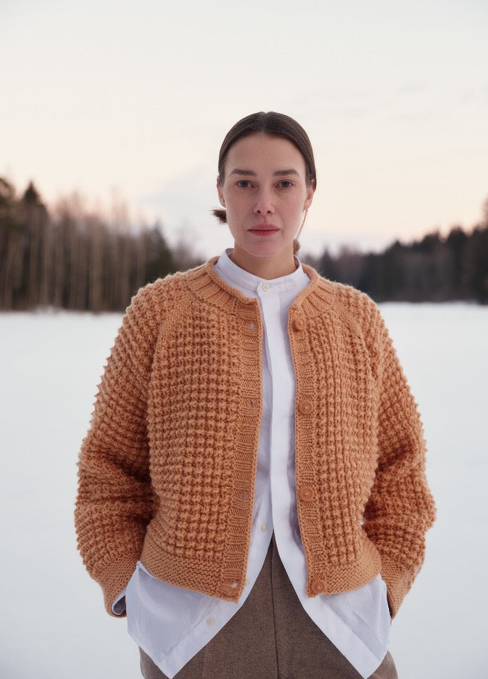 Textured cork-colored knit cardigan with front buttons, worn over a white shirt in a snowy outdoor setting.