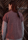Earth-toned textured cardigan shown from the back, with a ribbon-tied hairstyle against a wooden plank background.