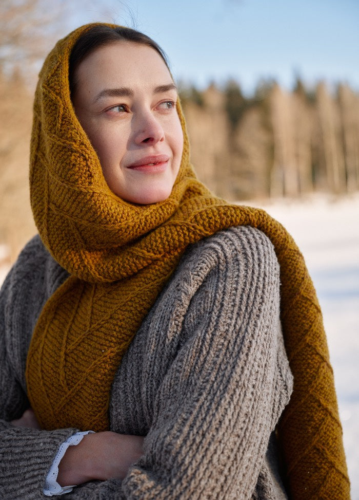 Mustard yellow knitted scarf wrapped around head and neck, styled with a grey sweater in a snowy outdoor setting.