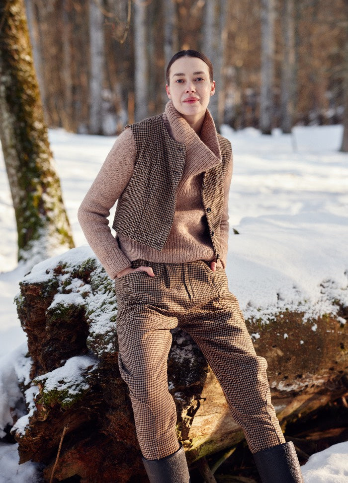 Brown and beige checkered sweater styled with matching pants and vest in a snowy forest setting.