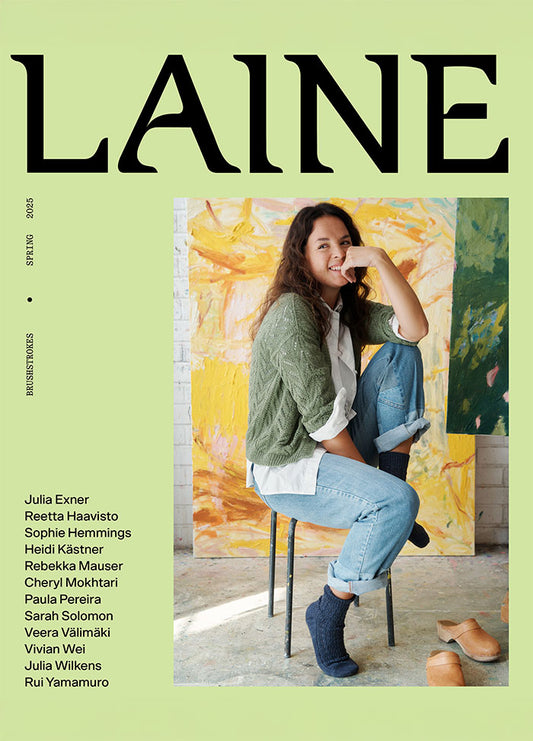 Cover of Laine Magazine Issue 24 featuring a seated model in a green sweater and jeans, with abstract art in the background.