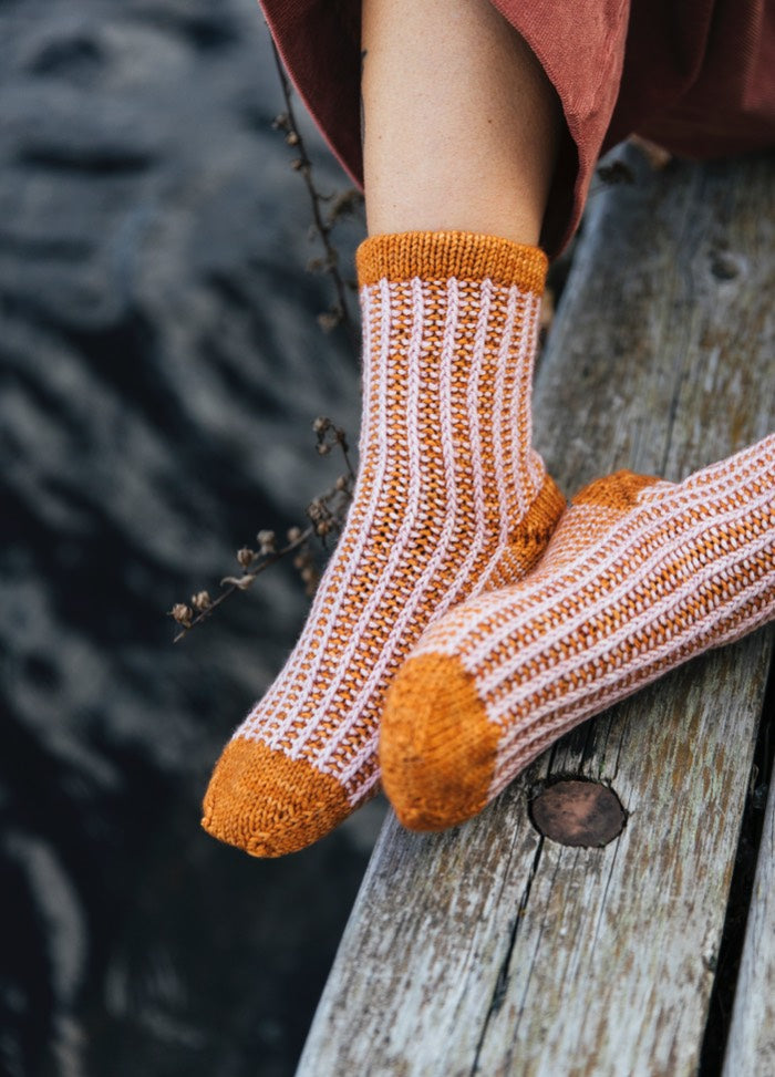 Wiklina Socks: orange and white striped knitted socks with solid orange cuffs, heels, and toes, worn near water.