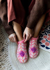 Juni Slippers: pink knitted slippers with purple and white patterns, worn on a woven rug with decorative mat accents.
