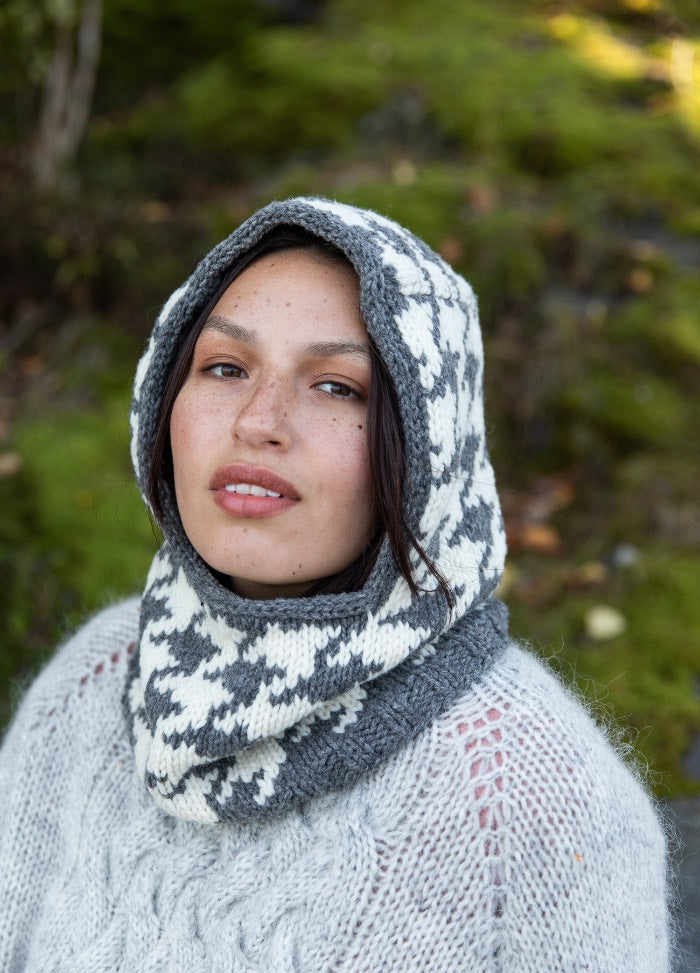 Cloudsteek Balaclava: white and gray houndstooth knit balaclava worn outdoors among green foliage and moss.