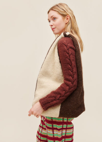 Bottari Bag: brown and white knit bag held by a model in a maroon cable sweater and colorful plaid pants.