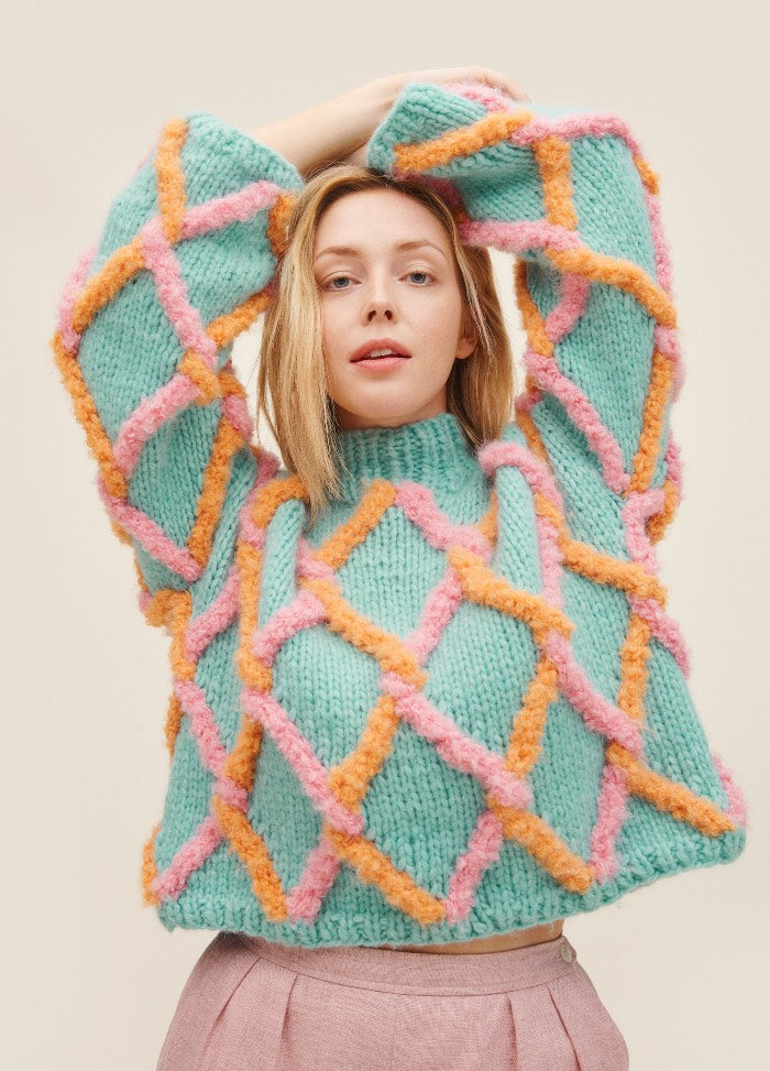 Net Sweater: light blue knit with pink and orange diamond mesh pattern, worn with light pink pants.