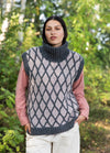 Jorvin Vest: light knit vest with dark diamond pattern and ribbed collar, layered over a pink shirt in a natural outdoor setting.