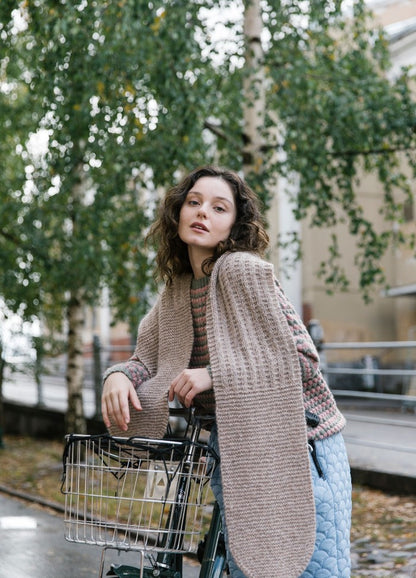 Abgerundet Scarf: knitted scarf draped over shoulders and arms, worn with striped sweater and quilted pants