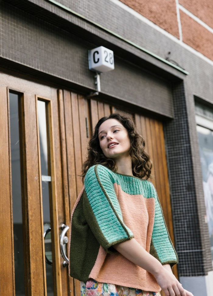 Cite Sweater: green and peach color-blocked knit worn in front of a wooden door with glass panels