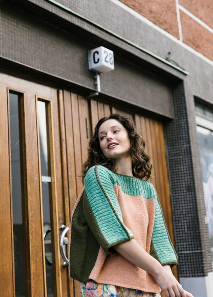 Cite Sweater: green and peach color-blocked knit worn in front of a wooden door with glass panels