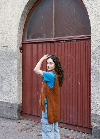 Witre Vest: brown knitted vest over a blue shirt with light blue cargo jeans in front of a wooden arched door