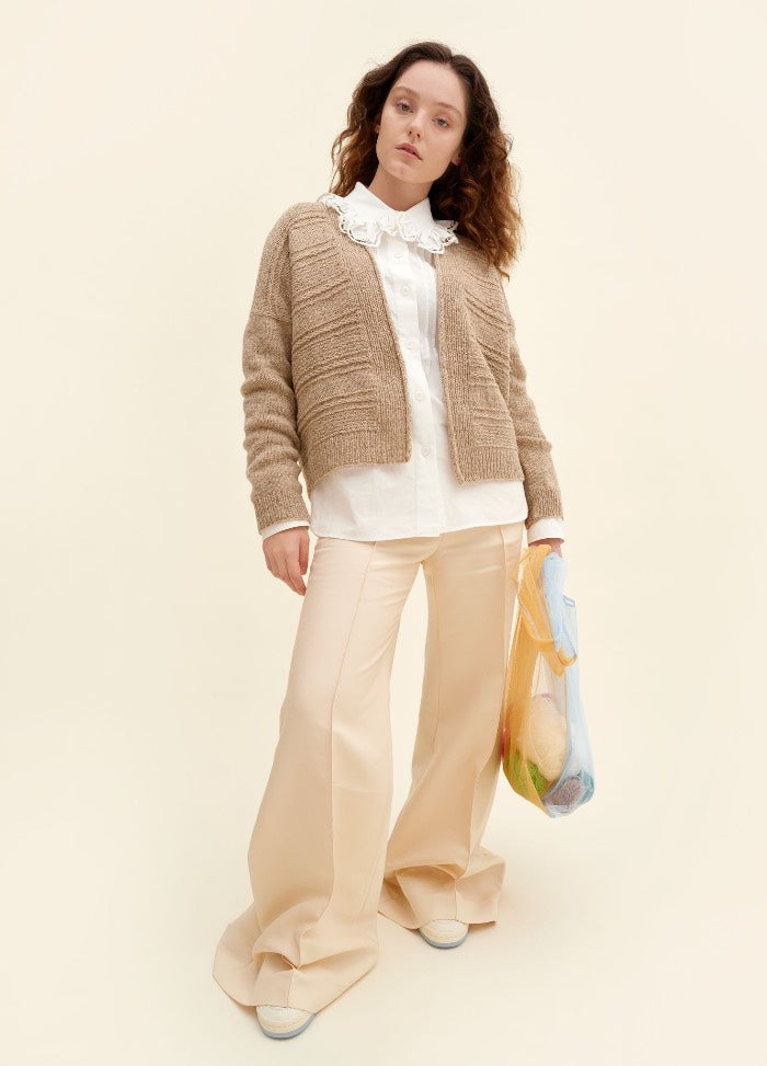 Juttu Cardigan: beige knit cardigan over a ruffled white blouse, paired with light pants and white shoes
