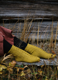 Craspedia Socks: mustard yellow textured socks worn with black leggings and pink pants, seated on dry grass and wooden planks