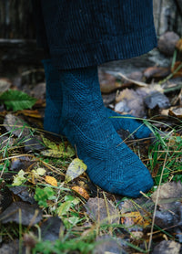 Suokatu Socks: blue textured wool socks worn with rolled-up dark pants, standing on grass and fallen leaves