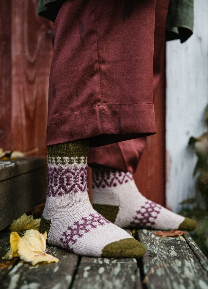 Boyland Socks: green, purple, and beige patterned socks worn with red pants, standing on wooden surface with fallen leaves