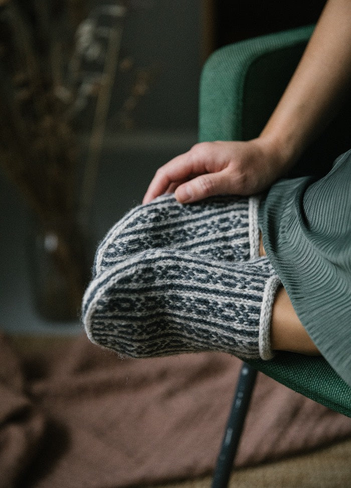 Elve Slippers: patterned knitted slippers worn while sitting on green chair, with dried plants and fabric in background
