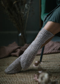 3 Leaves Socks: light brown knee-high socks with intricate leaf pattern, worn while seated with leg crossed over textured rug