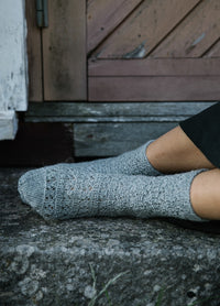 Rocking Chair Socks: gray lace-patterned knitted socks worn while resting feet on stone step in front of wooden door