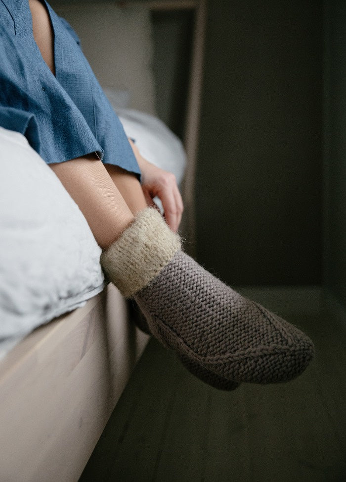 Carapins Slippers: gray knitted slippers with light fluffy cuffs, worn while sitting on bed with one foot on the floor