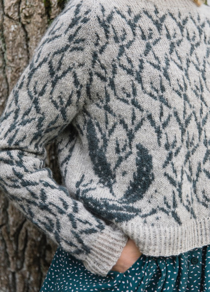 Crowfeet Sweater: light gray knit with dark crowfeet motifs, paired with teal speckled skirt.