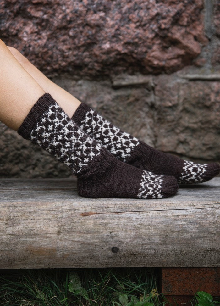 Olga Socks: dark brown knit with white geometric pattern, shown worn seated on wood.