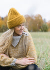 Hiesu Hat: mustard yellow knit worn outdoors with matching sweater and autumn trees.