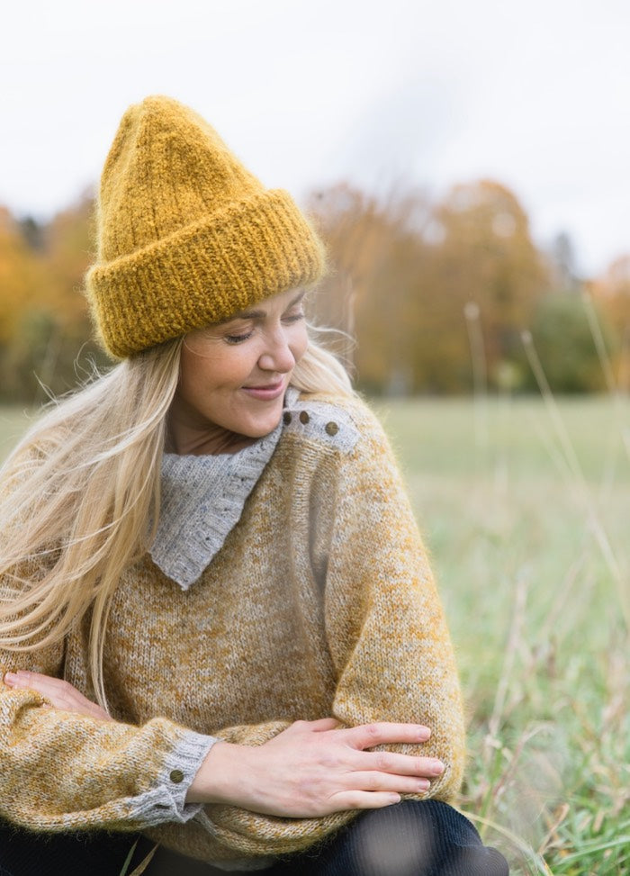 Hiesu Hat: mustard yellow knit worn outdoors with matching sweater and autumn trees.
