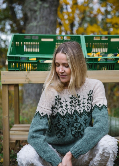 Magia Naturali Sweater: beige and dark green knit with tree motifs, worn outdoors near crates of produce.