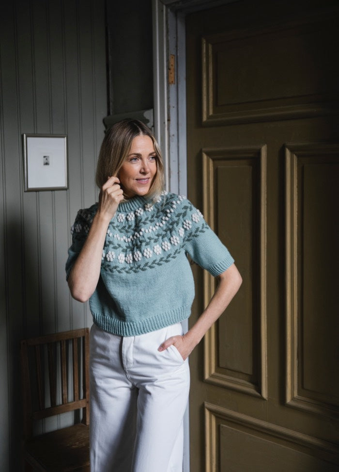 Vuokko Sweater: light blue knit with patterned yoke, worn indoors with white pants.