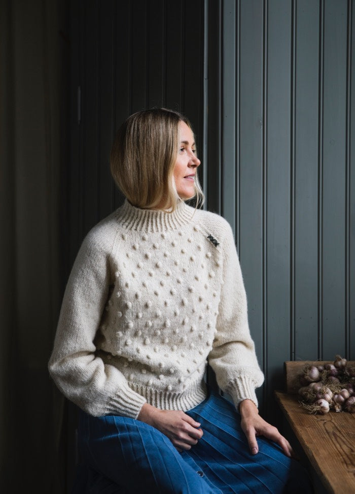 Nietos Sweater: cream knit with raised dot texture and ribbed neckline, shown seated indoors.