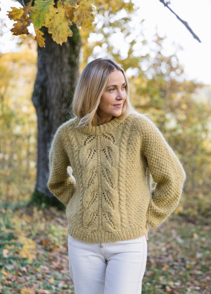 Hunaja Sweater: light yellow cable-knit worn outdoors with white pants and autumn trees.