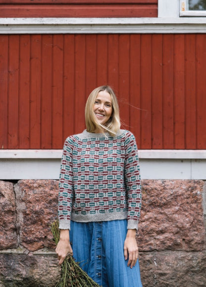 Ruutuloikka Sweater: geometric knit in grey, red, and blue, paired with blue buttoned skirt.