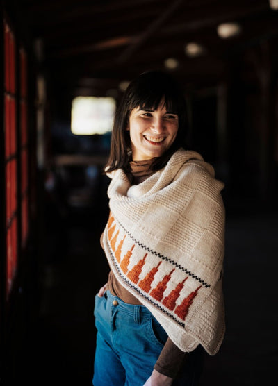 White shawl with orange and red patterned border, worn indoors with soft window light.