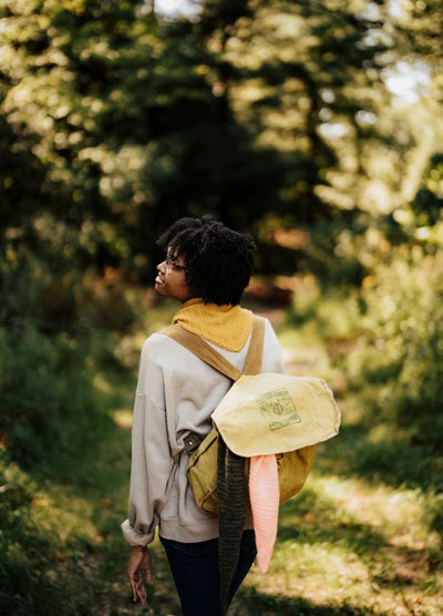 Yellow kerchief worn with a light sweatshirt and matching backpack on a forest trail.