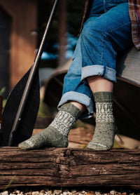 Green and white patterned socks worn with rolled-up jeans on a wooden dock beside a paddle.