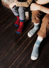 Red and blue socks on a child and blue and white socks on an adult, seated on a wooden floor.