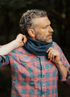 Blue knitted cowl worn with a red and blue plaid shirt in a forest setting.