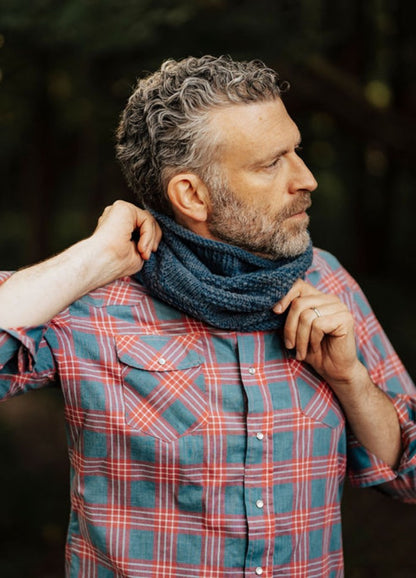 Blue knitted cowl worn with a red and blue plaid shirt in a forest setting.