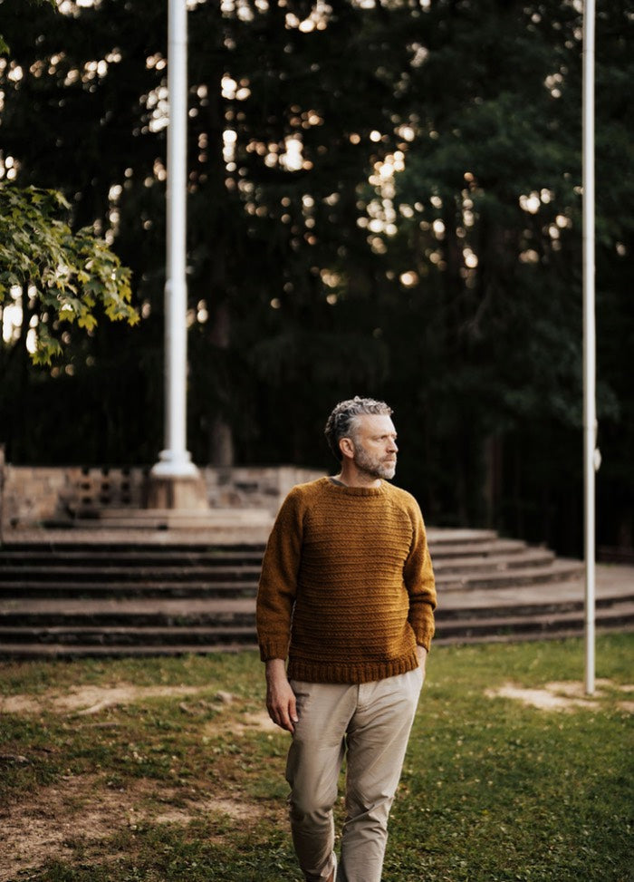 Brown sweater worn with beige pants on a grassy area with steps and flagpoles.