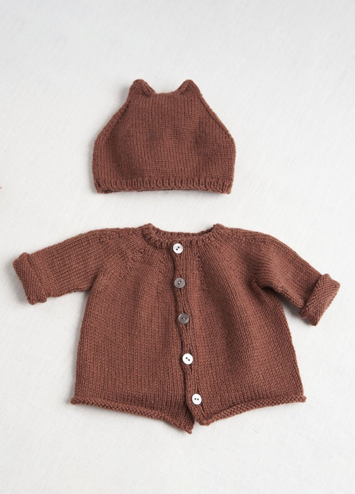 Brown knitted baby set on white surface, featuring a hat with tiny ears and a cardigan with white buttons, creating a cozy, warm vibe.