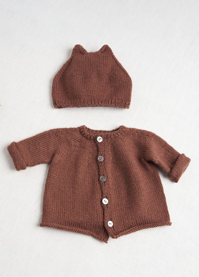 Brown knitted baby set on white surface, featuring a hat with tiny ears and a cardigan with white buttons, creating a cozy, warm vibe.