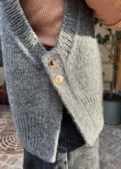 Close-up of a grey knit vest with brown buttons, worn over a ribbed brown sweater.