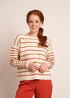 A woman wearing a cozy, multicolored striped knit sweater paired with vibrant red pants, standing confidently.