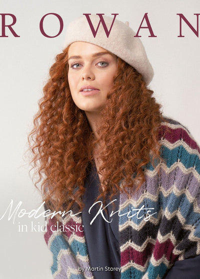 A close-up of a woman with long, curly red hair wearing a light beige beret and a pastel zigzag-patterned knit sweater, with the word "ROWAN" partially visible in large letters above.