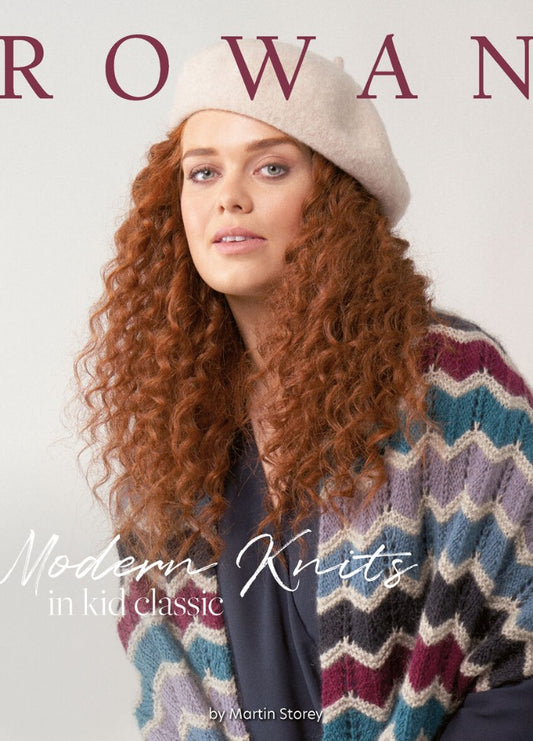 A close-up of a woman with long, curly red hair wearing a light beige beret and a pastel zigzag-patterned knit sweater, with the word "ROWAN" partially visible in large letters above.